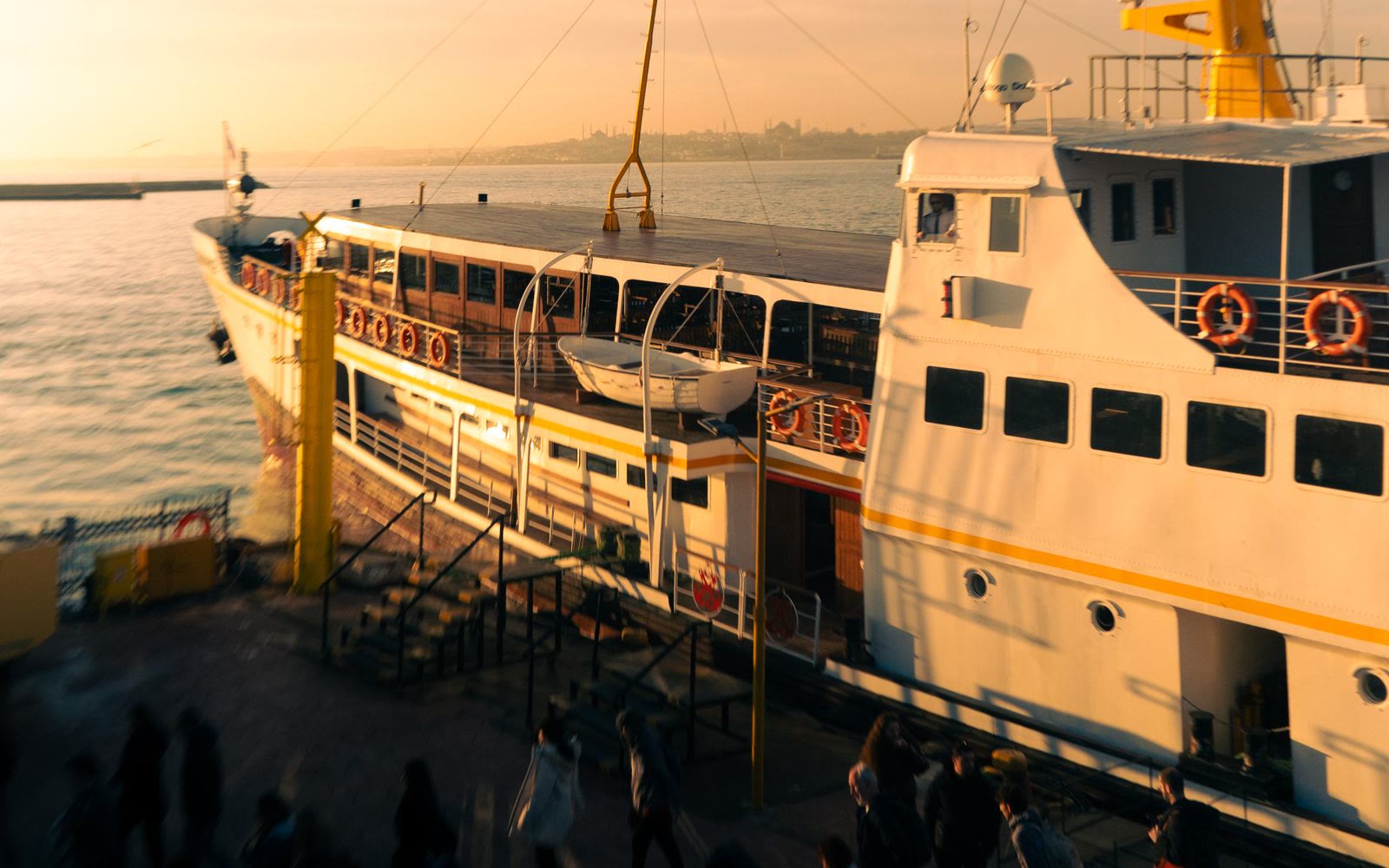 A passenger ferry docked at a harbor at golden-hour sunset, passengers boarding